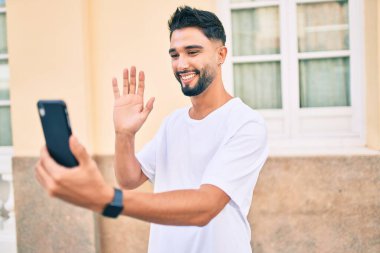 Genç Arap adam gülümseyerek şehirde akıllı telefon kullanarak video araması yapıyor..