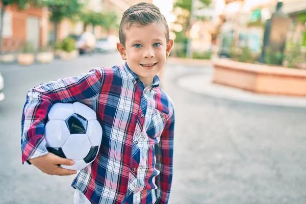 可爱的高加索男孩笑着高兴地拿着足球站在公园边 — 图库照片
