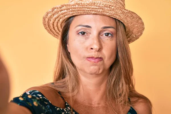 中年のヒスパニック女性が夏の帽子をかぶって自撮り懐疑的で緊張し 問題のために動揺して眉をひそめています 否定的な人 — ストック写真