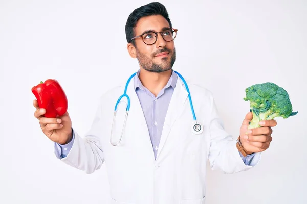 Jovem Hispânico Vestindo Estetoscópio Médico Segurando Pimenta Vermelha Brócolis Sorrindo — Fotografia de Stock