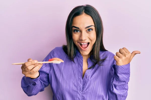 若いですブルネット女性食べる寿司で箸を指差す親指で側に笑顔幸せなでオープン口 — ストック写真