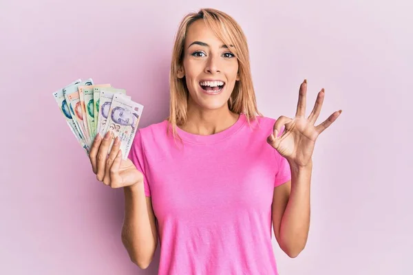 Beautiful Blonde Woman Holding Singapore Dollars Banknotes Doing Sign Fingers — Stock Photo, Image