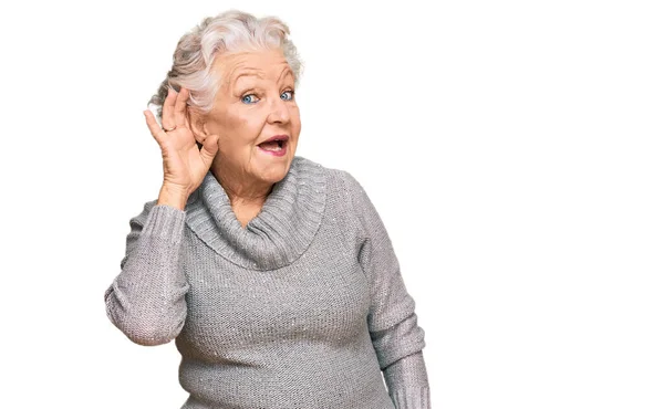 噂やゴシップに耳を傾ける耳の上に手で笑みを浮かべてカジュアルな冬のセーターを着てシニア白髪の女性 聴覚障害の概念 — ストック写真