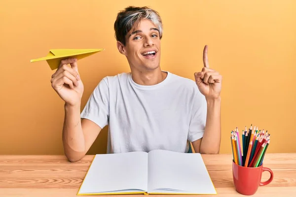 Młody Hiszpan Studiujący Trzymający Papierowy Samolot Siedzący Stole Uśmiechający Się — Zdjęcie stockowe