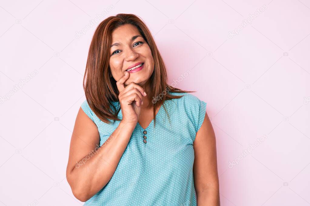 Middle age brunette hispanic woman wearing casual clothes looking confident at the camera with smile with crossed arms and hand raised on chin. thinking positive. 