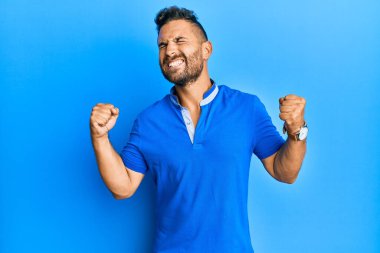 Sakallı yakışıklı, sıradan kıyafetler giyen, mutlu ve heyecanlı kolları havada, gülümseyen ve başarı çığlıkları atan, kazanan bir jest yapan bir adam. kutlama konsepti. 