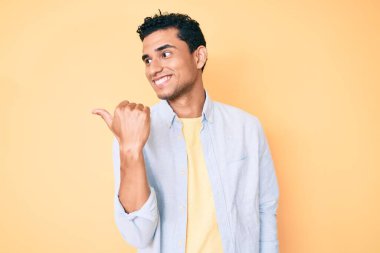 Sarı arka planda dikilen yakışıklı İspanyol adam baş parmağını yukarı kaldırıyor ve ağzı açık gülümsüyor. 