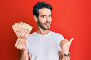 Meksika Pezosu 'nu elinde tutan genç İspanyol adam başparmağını yana kaldırmış, ağzı açık gülümsüyor. 