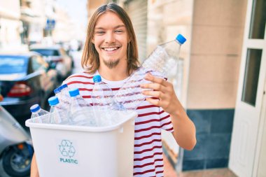 Sarışın, uzun saçlı ve sakallı beyaz bir adam plastik şişeleri geri dönüştürüyor.