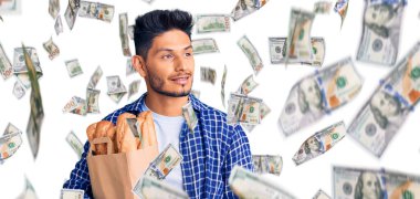 Yakışıklı Latin Amerikalı genç adam elinde ekmek torbasıyla gülümseyip yan tarafa bakıyor ve düşünüyor..