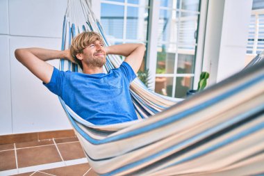 Orta yaşlı yakışıklı bir adam evinin terasında hamakta dinleniyor.