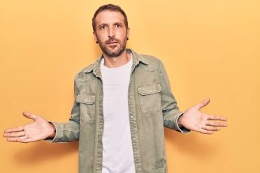 Sıradan kıyafetler giyen, elleri ve kolları havada, kafası karışmış genç ve yakışıklı bir adam. şüphe kavramı. 
