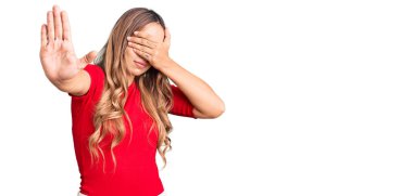 Genç, güzel, sarışın bir kadın. Günlük kıyafetler giyip, elleriyle gözlerini kapatıyor ve üzgün ve korku ifadeleriyle jest yapıyor. utangaç ve olumsuz kavram. 