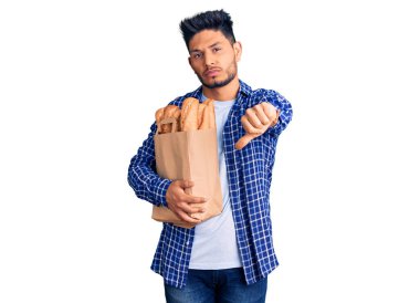 Elinde ekmek torbası olan yakışıklı Latin Amerikalı genç adam. Mutsuz ve sinirli görünüyor. Reddedildiğini gösteriyor. kötü ifade. 