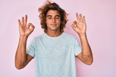 Günlük kıyafetler giyen genç İspanyol adam rahatla ve gözleri kapalı gülümse parmaklarıyla meditasyon hareketi yapıyor. yoga konsepti. 