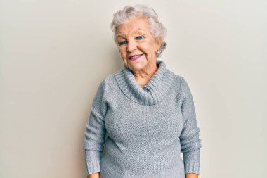 Yaşlı, gri saçlı, sıradan kıyafetler giyen, yüzünde mutlu ve havalı bir gülümseme olan bir kadın. şanslı kişi. 