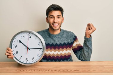 Büyük saat tutan yakışıklı genç adam gururla bağırıyor, zaferi kutluyor ve başarıyı kollarını kaldırarak kutluyor. 