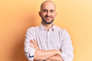 Zarif tişört giyen, kollarını kavuşturup kameraya bakarken gülümseyen kel, yakışıklı bir adam. pozitif kişi. 