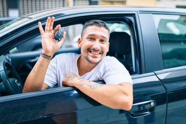Yeni arabanın anahtarını tutarken mutlu gülümseyen İspanyol genç adam.