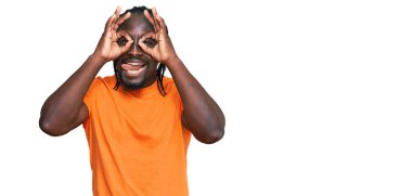 Yakışıklı, Afro-Amerikalı, günlük kıyafetler giyen, dürbün gibi jest yapan, dilini dışarı çıkaran, gözleriyle parmaklarından bakan bir adam. çılgın ifade. 