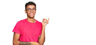 Genç, yakışıklı, Afro-Amerikalı, günlük kıyafetler giyen, gülümseyen, mutlu, eli ve parmağı yanda olan bir adam. 