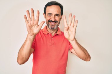 Orta yaşlı İspanyol bir adam gündelik kıyafetler giyip dokuz numaralı parmaklarıyla işaret ederken kendine güvenen ve mutlu bir şekilde gülümsüyor.. 