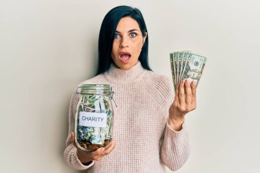 Elinde sadaka kavanozu ve dolar banknotları tutan genç beyaz kadın şaşkınlık ve şaşkınlık dolu bir ifade, korku ve heyecan dolu bir yüz ifadesi ile parlıyor.. 