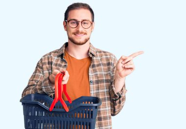 Süpermarket alışveriş sepeti tutan yakışıklı beyaz adam mutlu bir şekilde elini ve parmağını kenarda gezdiriyor. 