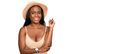 Yüzünde kocaman bir gülümseme olan, el ve parmak ile kameraya bakan, yaz şapkası takan genç siyahi kadın.. 