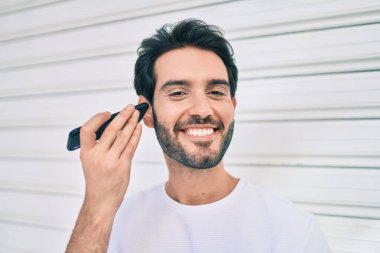 Genç İspanyol adam gülümsüyor. Şehirdeki akıllı telefonu kullanarak mutlu bir sesli mesaj dinliyor..