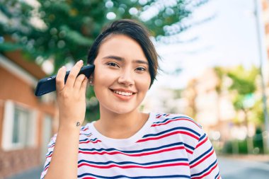Genç Latin kız gülümsüyor. Şehirdeki akıllı telefonu kullanarak mutlu bir sesli mesaj dinliyor.