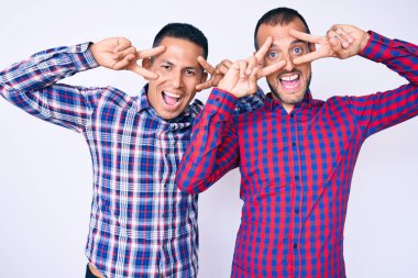 Genç eşcinsel iki adam, günlük kıyafetler giyip barış sembolü yapıyorlar. Yüzlerinde parmakları, gülümseyerek zaferlerini gösteriyorlar. 