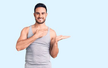 Mayo ve kolsuz tişört giyen genç yakışıklı adam kameraya hayret ediyor ve gülümsüyor.. 