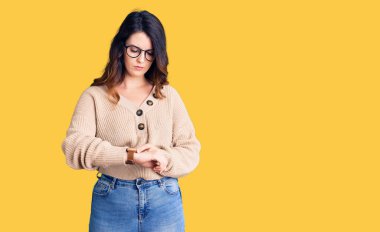 Güzel, genç, esmer bir kadın, günlük kıyafetler ve gözlük takıyor. Saati kontrol ediyor, rahat ve kendinden emin. 