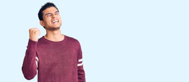 Hispanik yakışıklı genç adam rahat kıyafetler giyiyor kızgın ve kızgın yumruğunu kaldırıyor ve öfkeyle bağırıyor. öfke ve agresif konsept. 