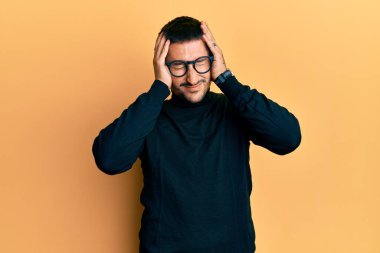 Boğazlı kazak giyen ve baş ağrısı çeken, çaresiz ve stresli gözlüklü yakışıklı bir adam. Ağrı ve migren yüzünden. Eller başının üstünde.. 