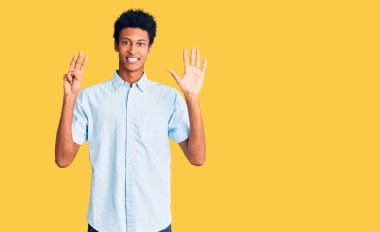 Genç, Afro-Amerikalı, günlük giysiler giymiş, 8 numaralı parmaklarıyla işaret ederken, kendinden emin ve mutlu bir şekilde gülümsüyor.. 