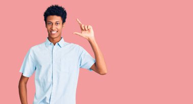 Gündelik kıyafetler giyen, gülümseyen, kendine güvenen, el hareketi yapan, parmaklarıyla işaret yapan ve kameraya bakan genç Afro-Amerikan bir adam. ölçüm kavramı. 