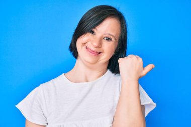 Down sendromlu esmer kadın, günlük kıyafetler giyip baş parmağını kaldırıyor ve ağzı açık gülümsüyor. 