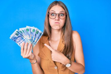 Güney Afrika rand banknotları tutan genç sarışın kız komik yüzlü yanakları şişiriyor. Ağzı havayla şişer, havayı yakalar.. 