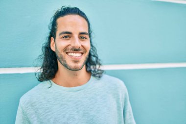 Genç İspanyol adam gülümsüyor. Duvara yaslanmış kameraya bakıyor.