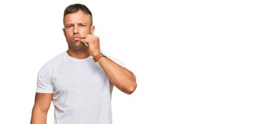 Beyaz tişört giyen yakışıklı kaslı adam ağzı ve dudakları parmaklarıyla kapalı. gizli ve sessiz, tabu konuşması 