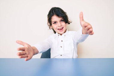 Masada oturmuş kucaklaşmak için kollarını açıp kameraya gülümseyen gündelik kıyafetler giyen tatlı İspanyol çocuk. Mutluluğu kucaklayan neşeli bir ifade.. 