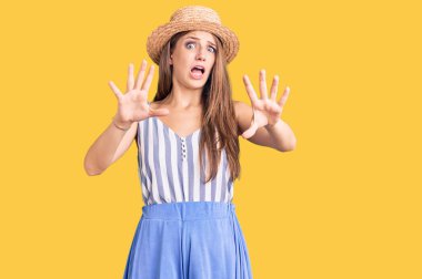 Yaz şapkası takan genç, güzel sarışın kadın korkudan dehşete düşmüş ve dehşete düşmüş. El hareketlerini bırak, şok içinde bağır. panik konsepti. 