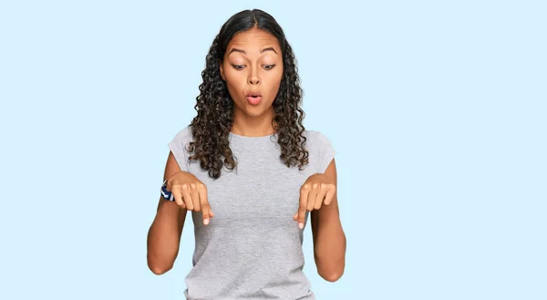 穿着休闲装的年轻的非洲裔美国女孩 手指垂下 露出广告 惊讶的脸和张开的嘴 — 图库照片