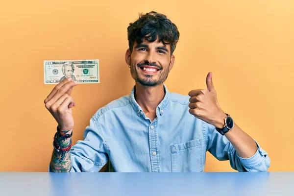 Fiatal Spanyol Férfi Kezében Dolláros Bankjegy Mosolyog Boldog Pozitív Hüvelykujj — Stock Fotó