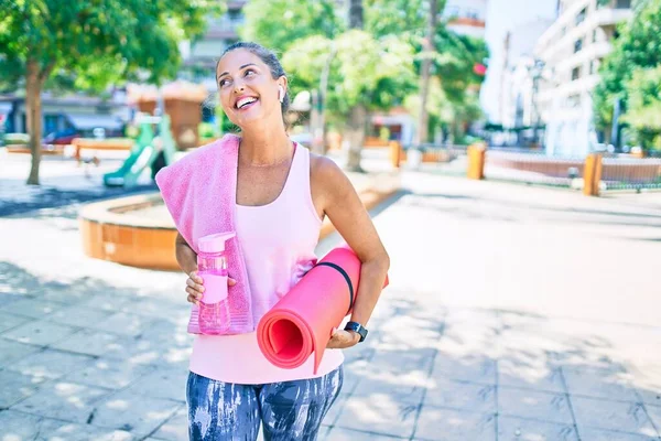 中年妇女带着瑜伽垫和一瓶水在公园里开心地笑着 — 图库照片
