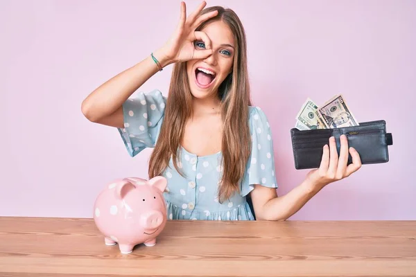 Jong Blond Meisje Holding Portemonnee Met Dollars Spaarvarken Bank Zitten — Stockfoto