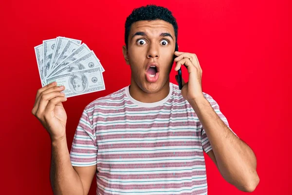 Genç Arap adam elinde dolarlarla akıllı telefonla konuşuyor. Şaşırmış ve şaşırmış bir ifade, korku ve heyecanlı bir yüz ifadesi var.. 