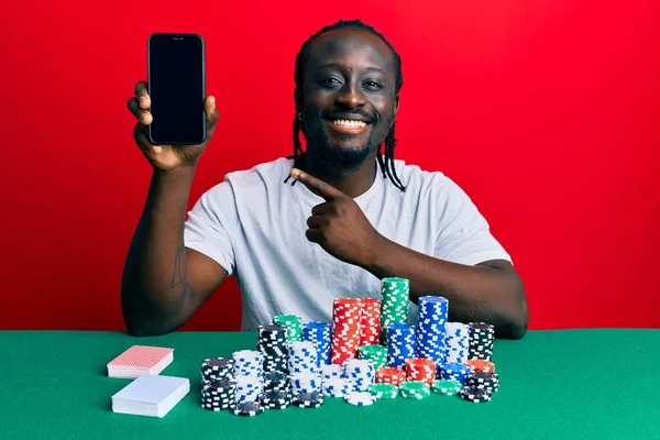 Bonito Jovem Negro Jogando Poker Segurando Smartphone Sorrindo Feliz Apontando — Fotografia de Stock